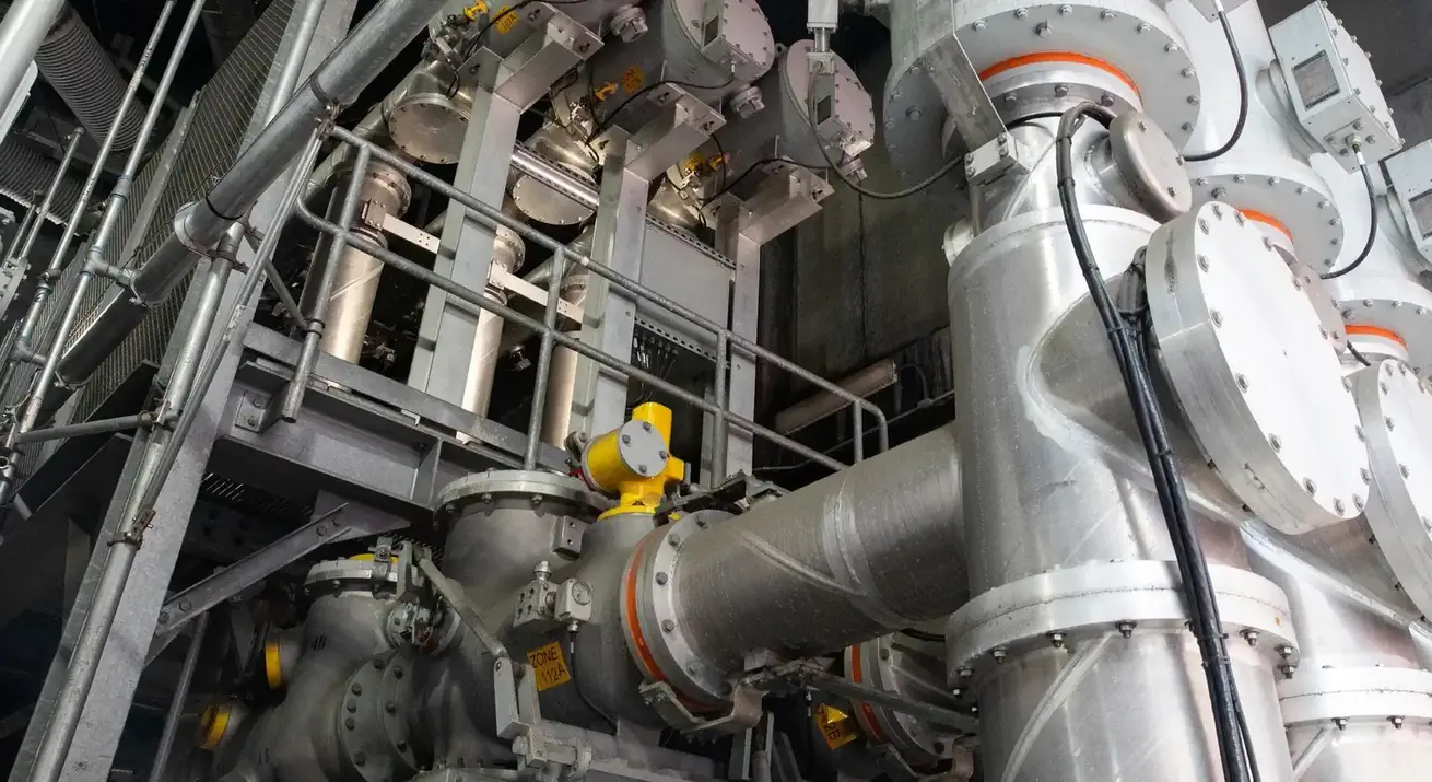 Tuberías industriales de cerca con anillos naranjas y un actuador amarillo