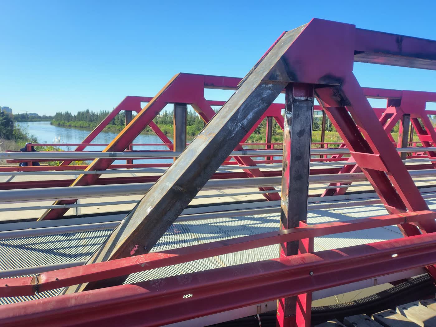 Puente reticulado metálico pintado de rojo con operario soldando en estructura